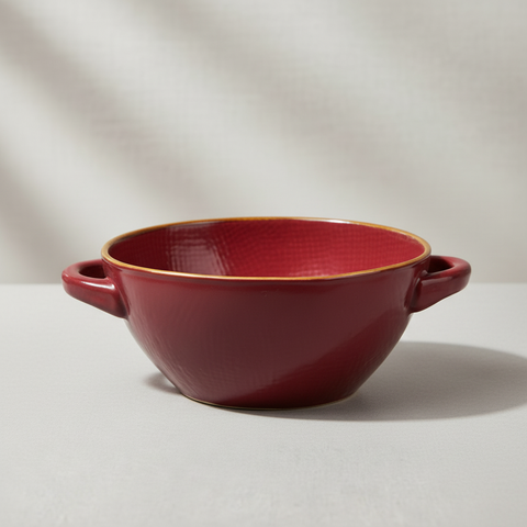 Ciotola ceramica rossa con manici e bordo oro su sfondo grigio con ombre