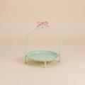 Alzatina verde menta con fiocco rosa su sfondo beige con ombra