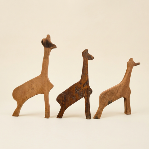 Tre giraffe in legno su sfondo avorio con ombre morbide